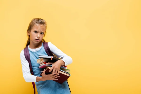 Sad schoolkid holding books and notebooks isolated on yellow — Stock Photo