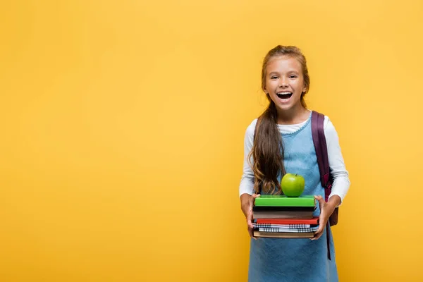 Alegre alumno sosteniendo libros y manzana aislada en amarillo - foto de stock