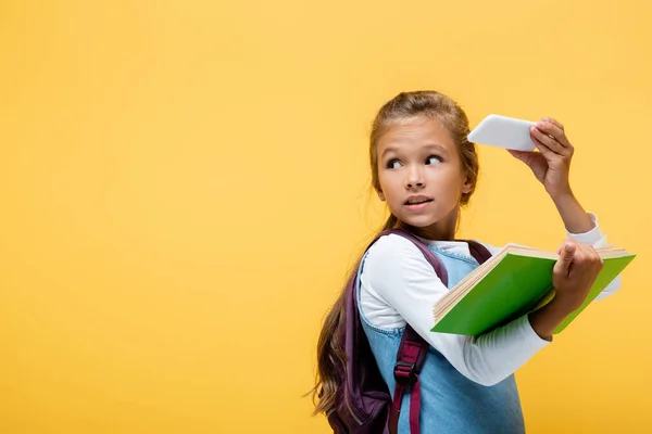 Schulkind hält Smartphone und Buch isoliert auf gelb — Stockfoto