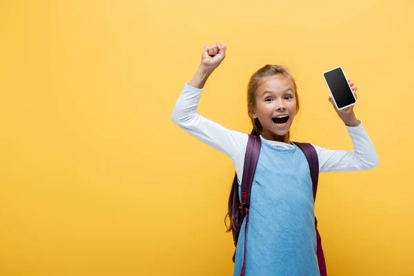 Emocionado colegial sosteniendo teléfono inteligente y mostrando sí gesto aislado en amarillo - foto de stock