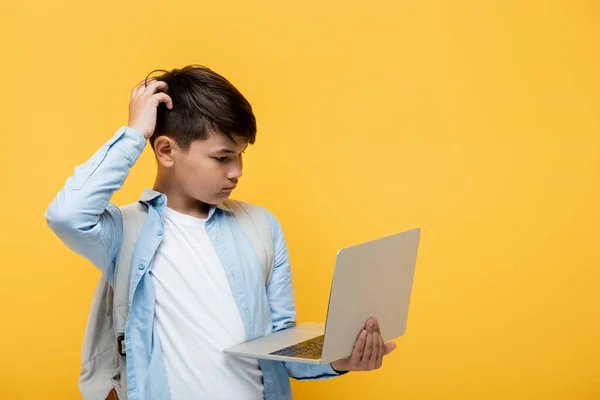 Pensive asian schoolboy looking at laptop isolated on yellow — Stock Photo