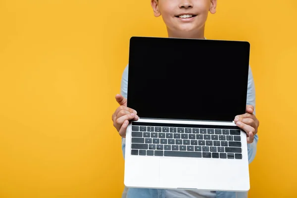 Обрізаний вигляд позитивного дев'ятнадцяти школяра тримає ноутбук ізольовано на жовтому — стокове фото