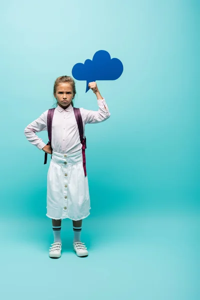 Angry schoolgirl holding thought bubble on blue background — Stock Photo