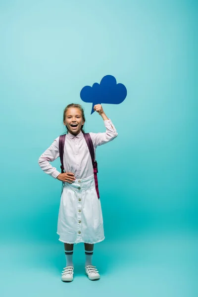 Cheerful schoolgirl holding thought bubble on blue background — Stock Photo
