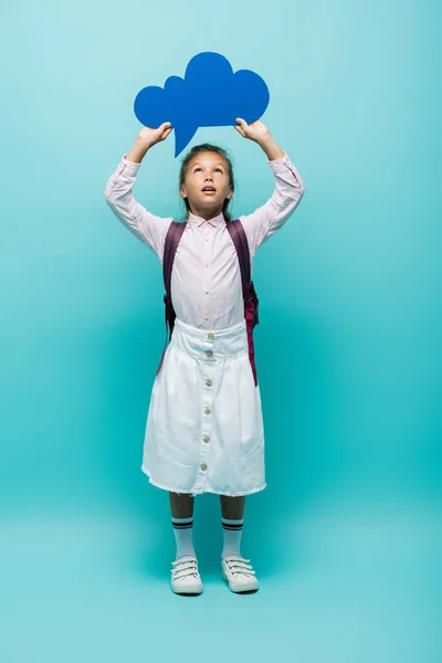 Full length of schoolgirl holding thought bubble on blue background — Stock Photo