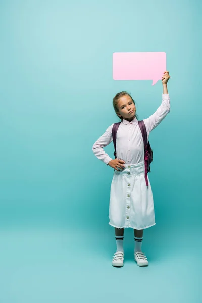 Skeptical schoolkid holding speech bubble on blue background — Stock Photo