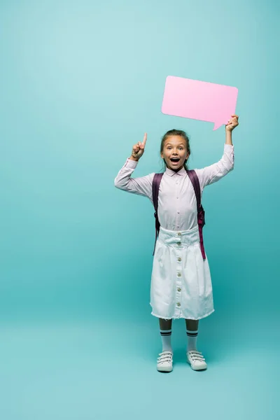 Emocionada colegiala sosteniendo la burbuja del habla y teniendo idea sobre fondo azul - foto de stock