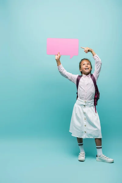 Lächelndes Schulkind zeigt auf Sprechblase auf blauem Hintergrund — Stockfoto