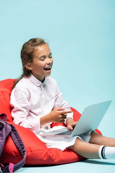 Lachende Schülerin zeigt auf Laptop auf blauem Hintergrund — Stockfoto