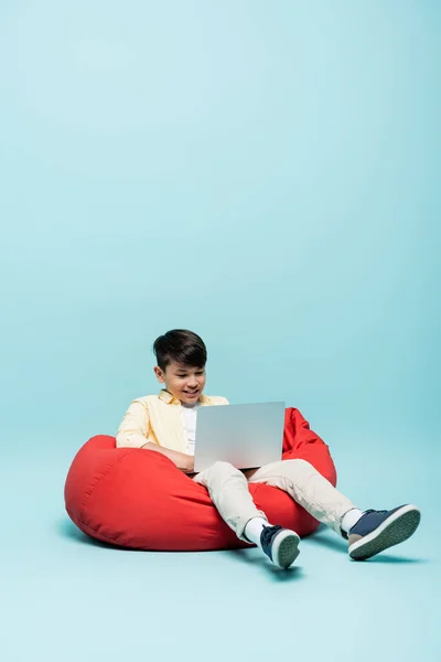 Sourire asiatique écolier à l'aide d'ordinateur portable sur fond bleu — Photo de stock