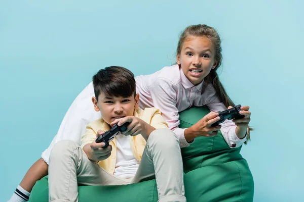KYIV, UKRAINE - JULY 2, 2021: Focused multiethnic kids playing video game isolated on blue — Stock Photo
