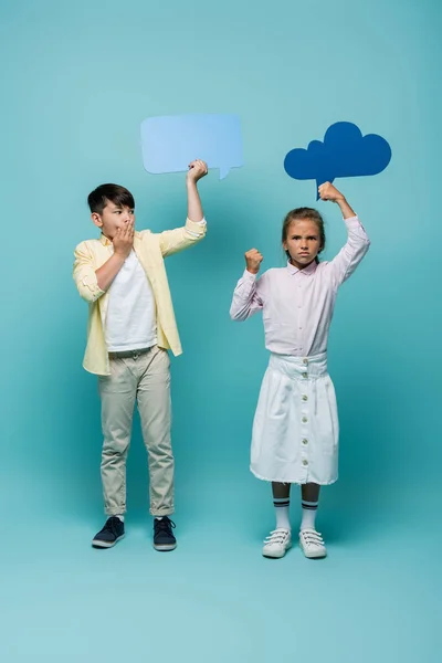 Agresiva colegiala celebración pensamiento burbuja cerca asustado asiático amigo en azul fondo - foto de stock