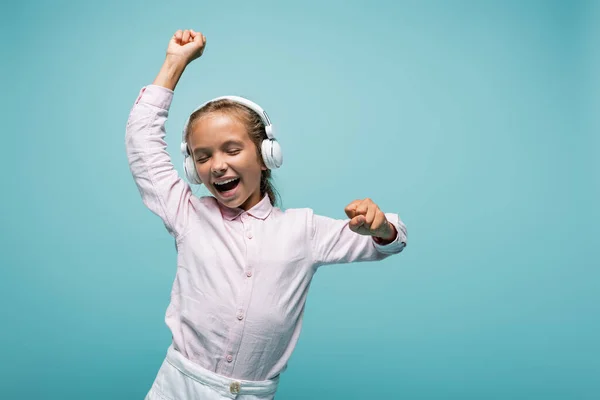 Cheerful schoolkid listening music in headphones isolated on blue — Stock Photo