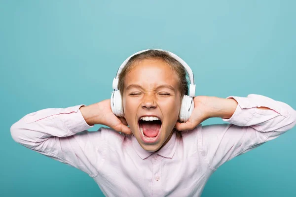 Angry preteen schoolgirl listening music in headphones isolated on blue — Stock Photo