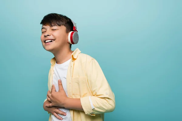 Feliz asiático escolar en auriculares sonriendo aislado en azul - foto de stock