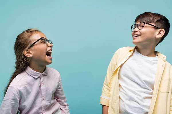 Smiling interracial preteen schoolkids in eyeglasses isolated on blue — Stock Photo