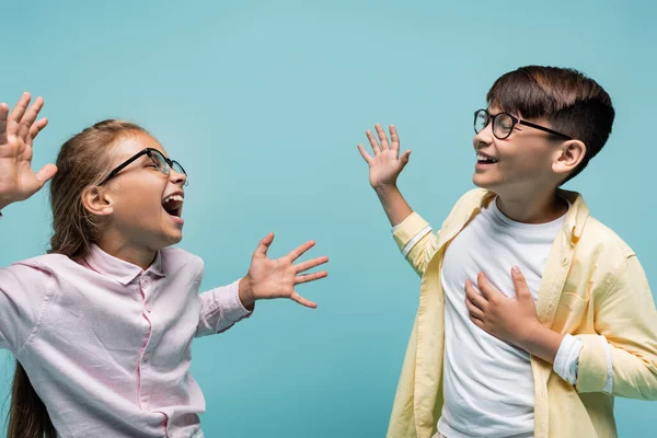 Los colegiales multiétnicos en gafas que se divierten aislados en azul - foto de stock