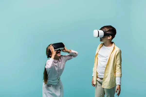 Alegre niño en auriculares vr jugando videojuego cerca de amigo aislado en azul - foto de stock