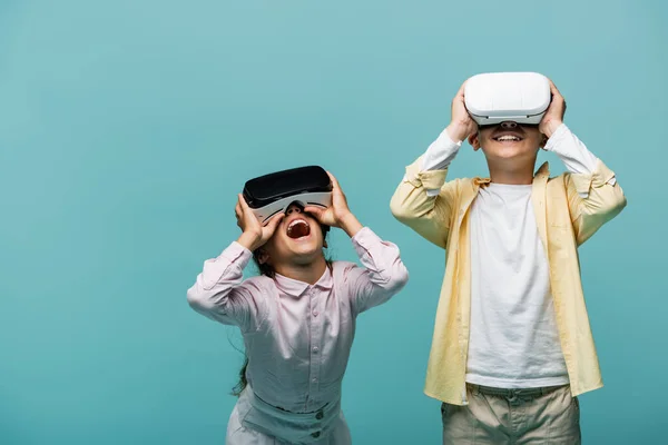 Excited preteen kids playing video game in vr headsets isolated on blue — Stock Photo