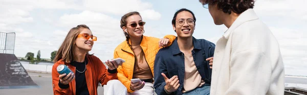 Feliz asiático hombre mostrando pulgar hacia arriba mientras pasar tiempo con jóvenes amigos al aire libre, bandera - foto de stock