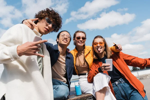 Amigos multiétnicos alegres mostrando sinais de rock e vitória enquanto se divertem ao ar livre — Fotografia de Stock
