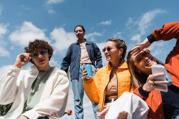 Happy young women with smartphone and soda can spending time with interracial friends outdoors — Stock Photo