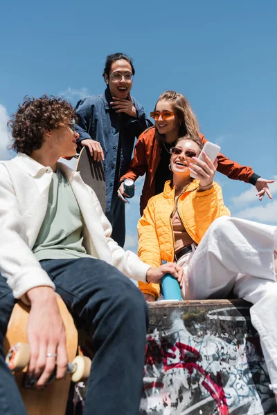 Tiefansicht einer jungen Frau, die ein Selfie mit multiethnischen Freunden vor blauem Himmel macht — Stockfoto