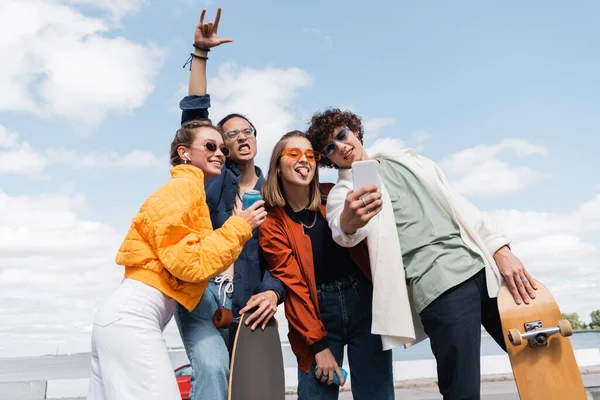 Asiatique patineur montrant signe de roche près excité amis prendre selfie à l'extérieur — Photo de stock