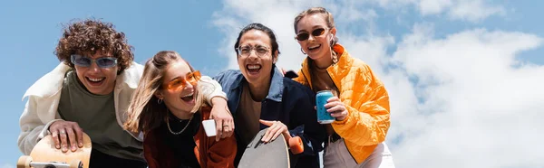 Vista de ángulo bajo de patinadores multiétnicos emocionados riendo al aire libre, pancarta - foto de stock