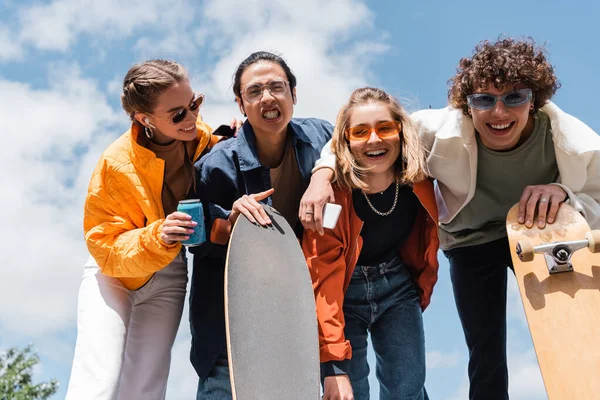 Asian skater grimacing near cheerful friends having fun outdoors — Stock Photo