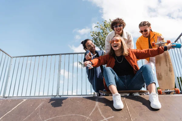 Excited woman with soda can screaming on ramp in skate park near interracial friends — Stock Photo