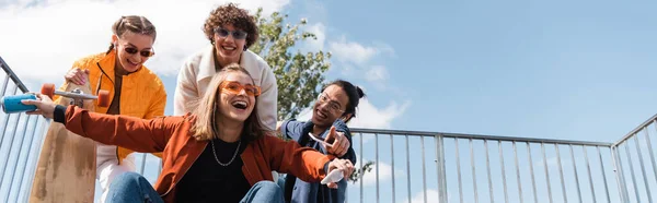 Mujer emocionada con refrescos puede gritar cerca de patinadores multiculturales, pancarta - foto de stock