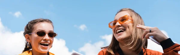 Молоді жінки в модних сонцезахисних окулярах посміхаються на блакитне хмарне небо, банер — стокове фото