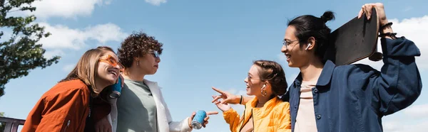 Smiling multicultural friends pointing at each other while talking outdoors, banner — Stock Photo