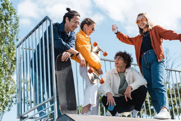 Joyeux patineurs multiethniques en vêtements à la mode parlant sur la rampe dans le skate park — Photo de stock