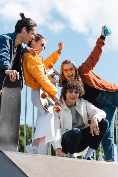 Asian skater pointing at overjoyed friends screaming with raised hands outdoors — Stock Photo