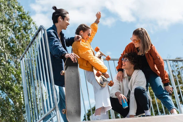 Mujer emocionada mostrando gesto de victoria cerca de patinadores multiétnicos en skate park - foto de stock