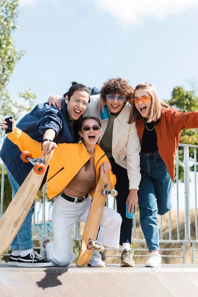 Patinadores interracial emocionados mirando a la cámara y gritando al aire libre — Stock Photo