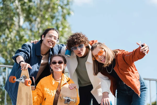 Patinadores multiculturales alegres en ropa de moda mirando a la cámara al aire libre — Stock Photo