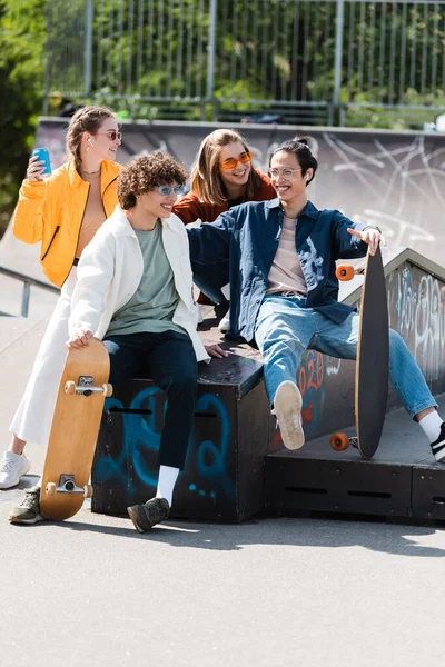 Amis multiethniques joyeux et branchés assis sur le rebord dans le skate park — Photo de stock
