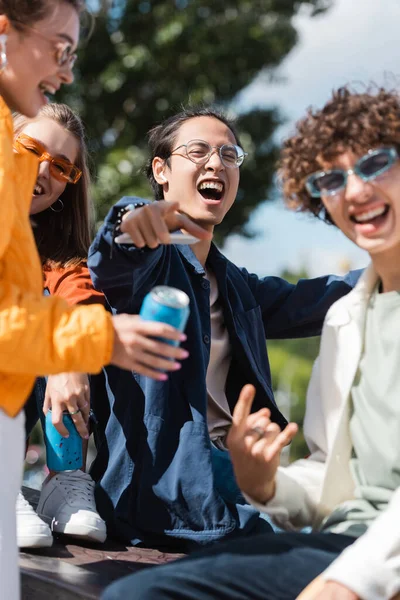 Eccitato asiatico uomo in occhiali puntando con dito vicino offuscata amici all'aperto — Foto stock