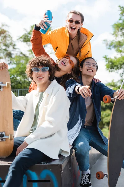 Aufgeregter asiatischer Mann zeigt mit dem Finger in die Nähe glücklicher Freunde mit Getränkedosen — Stockfoto