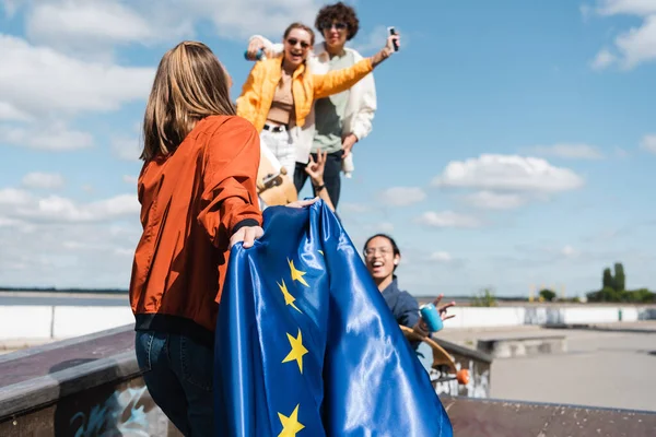 Молода жінка тримає прапор Єс поблизу розмитих мультикультурних друзів на відкритому повітрі — стокове фото