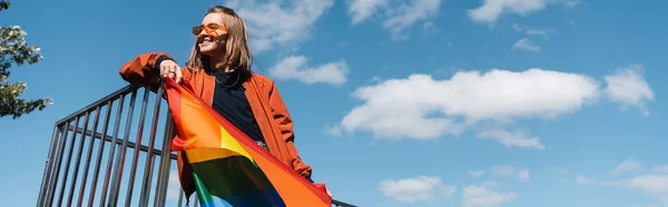 Mujer feliz en gafas de sol de moda sosteniendo lgbt orgullo bandera al aire libre, bandera - foto de stock