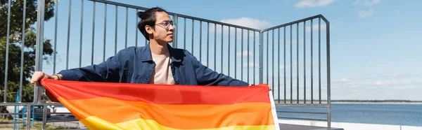 Asiatico uomo in occhiali tenendo lgbt bandiera e guardando lontano, striscione — Foto stock