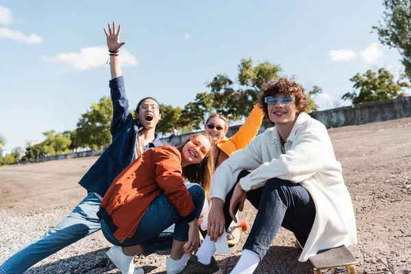 Excitada mujer asiática con la mano levantada gritando cerca sonriendo amigos al aire libre - foto de stock