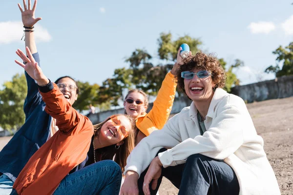 Alegres amigos multiétnicos en ropa de moda divertirse y mirando a la cámara al aire libre - foto de stock