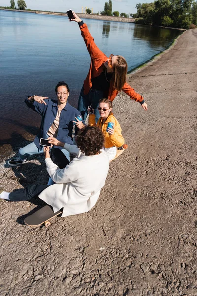 Feliz asiático hombre mostrando victoria signo mientras pasar tiempo con amigos cerca de lago - foto de stock