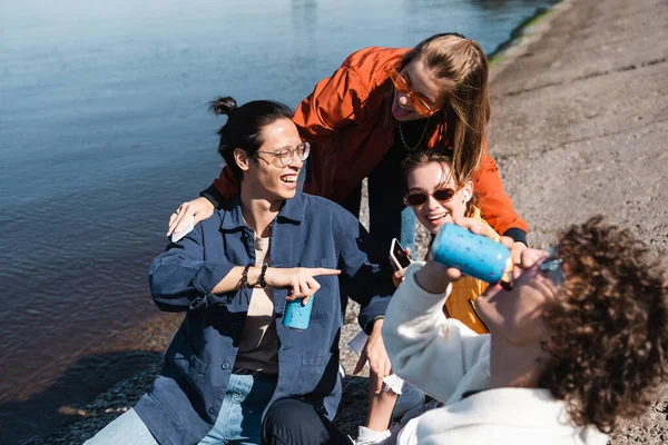 Borracho hombre beber soda cerca feliz multicultural amigos en terraplén - foto de stock