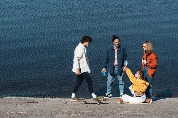 Full length of young multicultural skaters with soda cans on river bank — Stock Photo